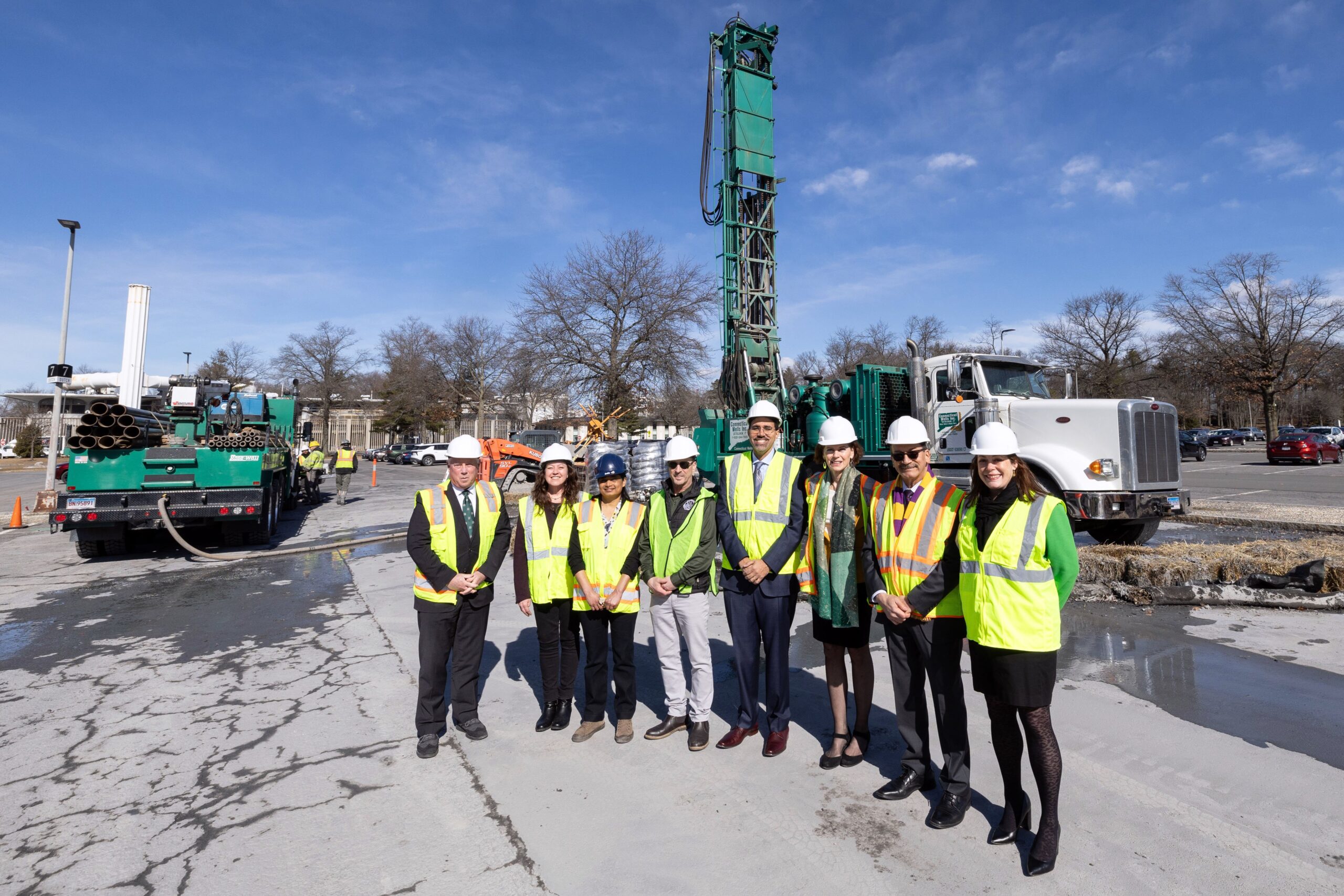 Construction works, both men and women, dressed in bright vests, stand at a worksite.