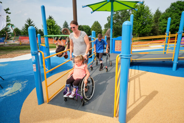 Where to Buy Custom Color Surfacing Materials for Playgrounds An inclusive playground with several children and adults making use of the colorful equipment.