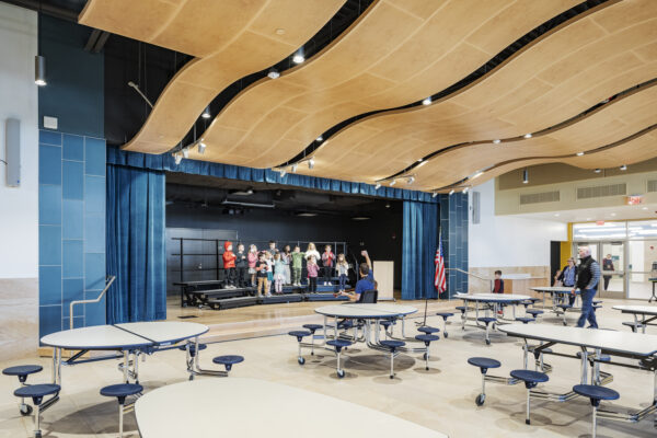 Florence Roche Elementary School Incorporates Universal Design for Learning, Reflects Local Landscape A multipurpose room features an wood ceiling with students performing in front of what appears to be both a gymnasium and a lunch room.