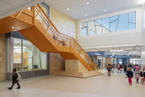 An orange stairwell takes up a bright school hallway.