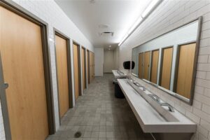 Interior restroom with wood paneling doors for private stalls, with a long communal sink.
