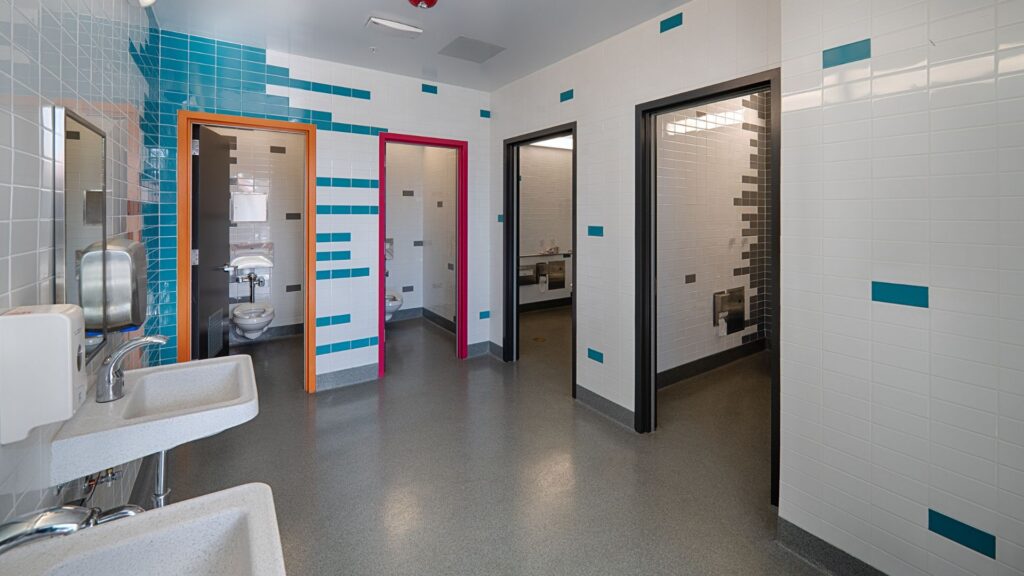 The inclusive restroom at Freestyle Academy in the Mountain View Los Altos Unified High School District shows that these layouts can often be achieved within the same building footprint as traditional restrooms, making them feasible for both new construction and renovation projects.